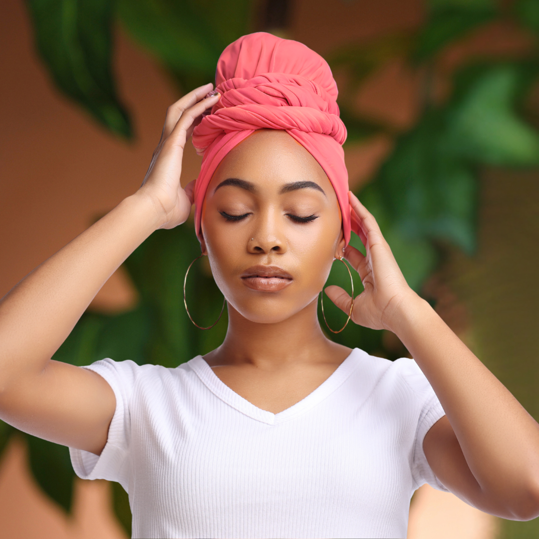 Woman adjusting a pink headscarf headwrap against a blurred green background